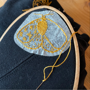Embroidery hoop with gold thread design on a dark fabric background. 