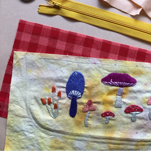Embroidered mushrooms on fabric with a yellow zipper and red checkered material in the background.