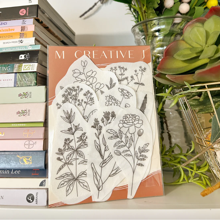 Embroidery supplies with natural dye plant  design on a surface with books and plants in the background. 