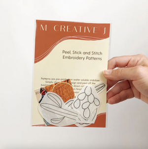 Hand holding a 'M Creative J' embroidery patterns pack of simple cactus transfers on a white background. 