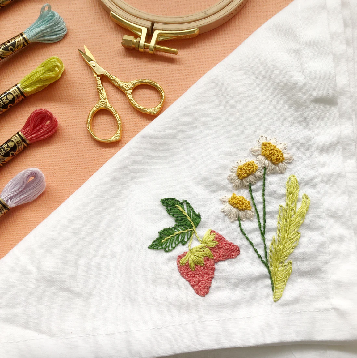 Embroidery hoop, scissors, and embroidery thread with a partially completed floral design on white fabric.