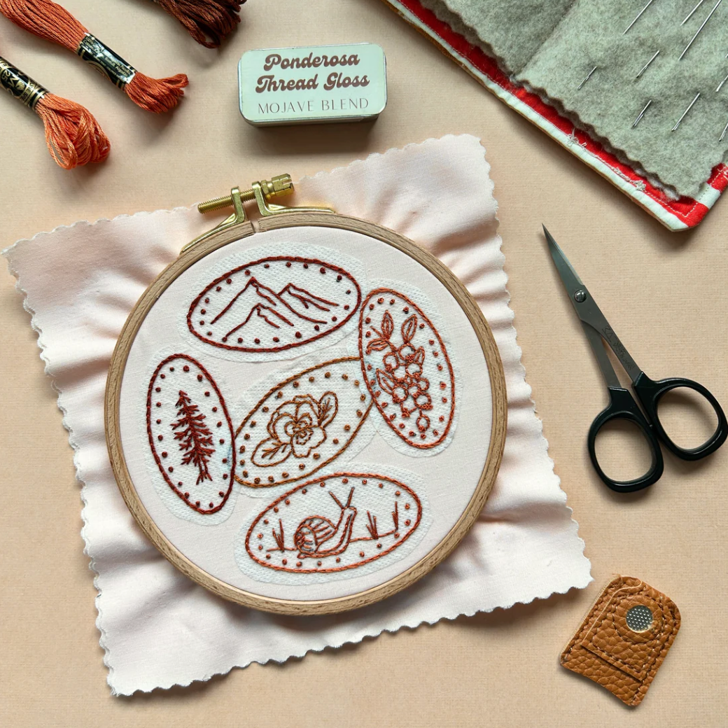 Embroidery hoop with pressed penny-themed design on a beige surface with embroidery tools.