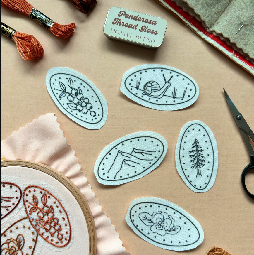 Embroidery transfers with pressed penny designs on a beige surface with embroidery tools.