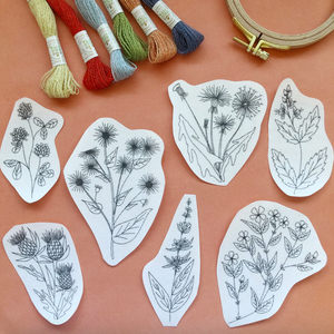 Embroidery patterns with floral designs on a peach-colored background, accompanied by embroidery threads and a hoop.