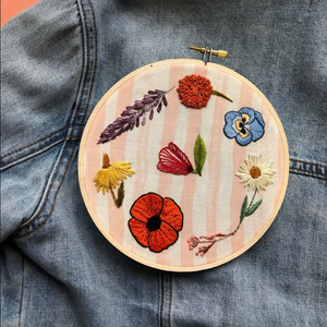 Embroidery hoop with colorful floral design on a denim background. 