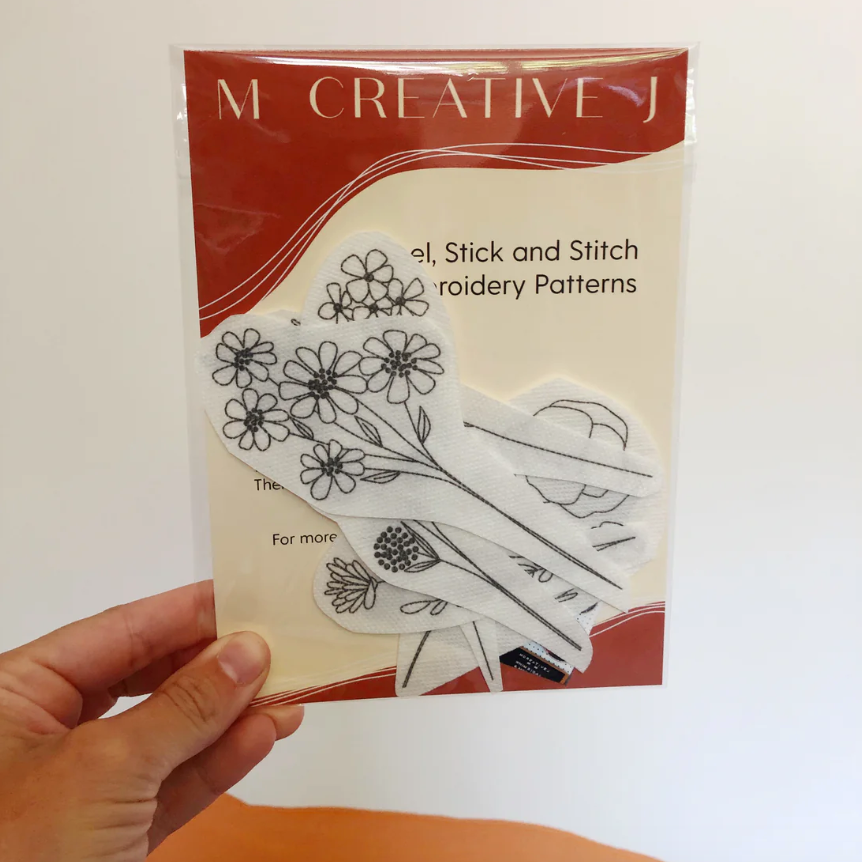 Hand holding a package of embroidery transfers by 'M Creative J' with wildflower stems theme. 