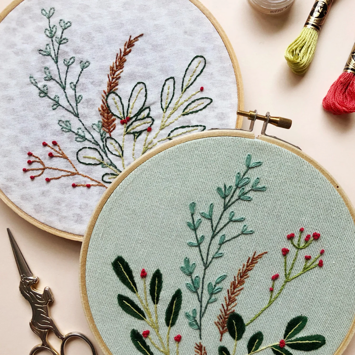 Embroidery hoops with floral patterns on a light surface, surrounded by embroidery tools.