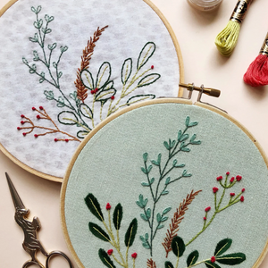 Embroidery hoops with floral patterns on a light surface, surrounded by embroidery tools.