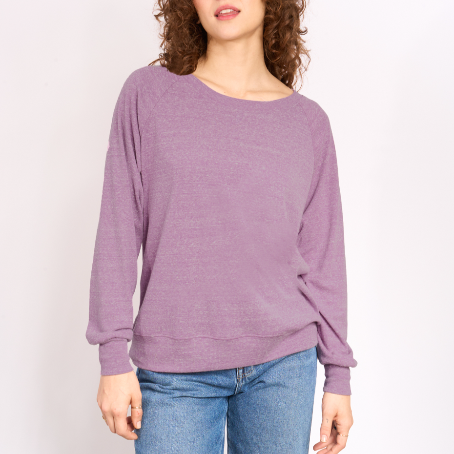 Woman wearing a purple sweater and blue jeans against a white background. 