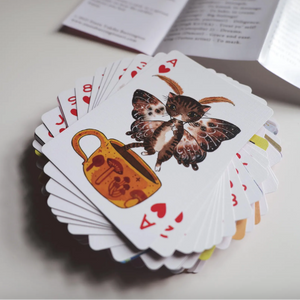 Playing cards with butterfly and teacup design on a light surface.
