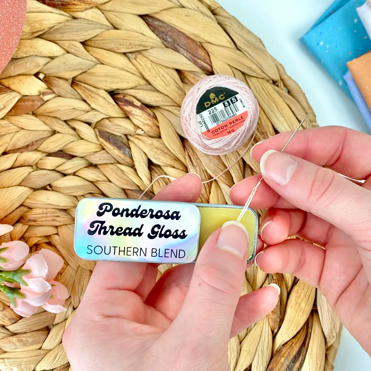 A metal tin of Ponderosa Thread Gloss - Southern Blend - against a background of folded fabrics, embroidery floss and a woven mat.