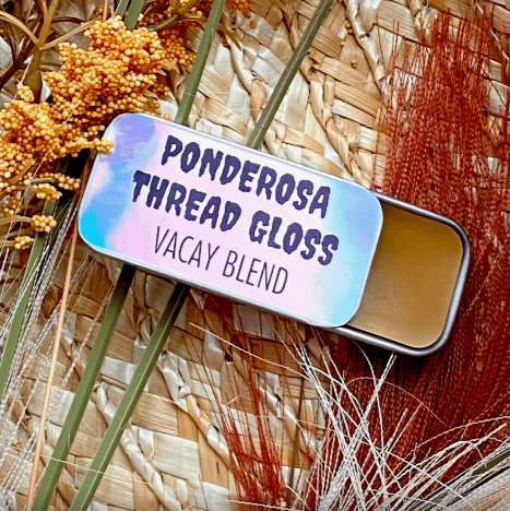 A metal tin of Ponderosa Thread Gloss - Vacay Blend - against a background of dried florals.