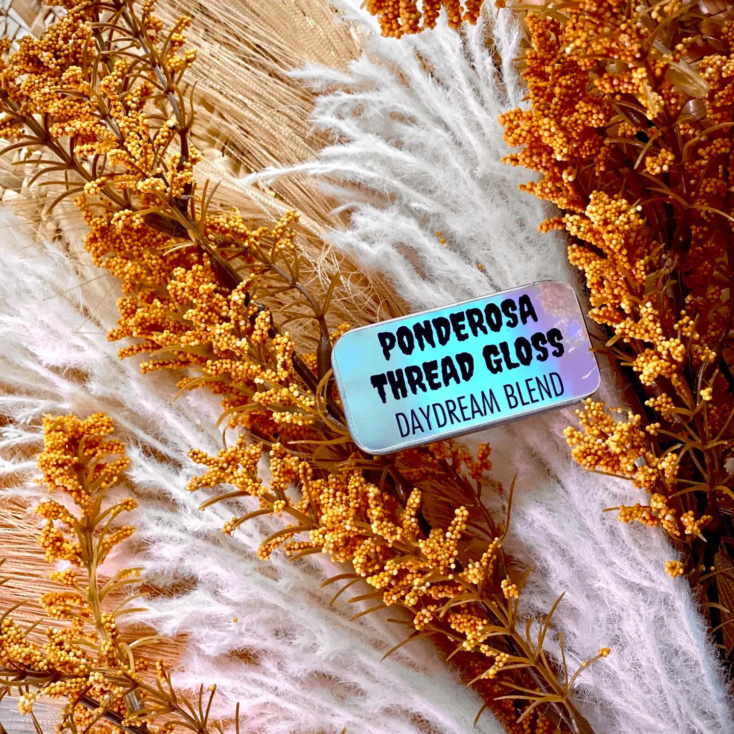 A tin of Ponderosa Thread Gloss - Daydream Blend - on the background of dried floral and wheat.