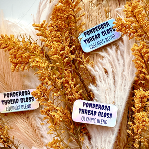 Several tins of Ponderosa Thread Gloss scattered against a background of dried flowers.