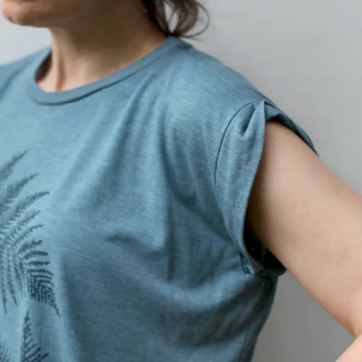 Person wearing a blue t-shirt with a fern design against a neutral background. 