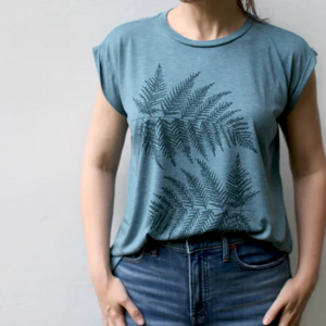 Person wearing a blue t-shirt with fern design and jeans against a plain background. 