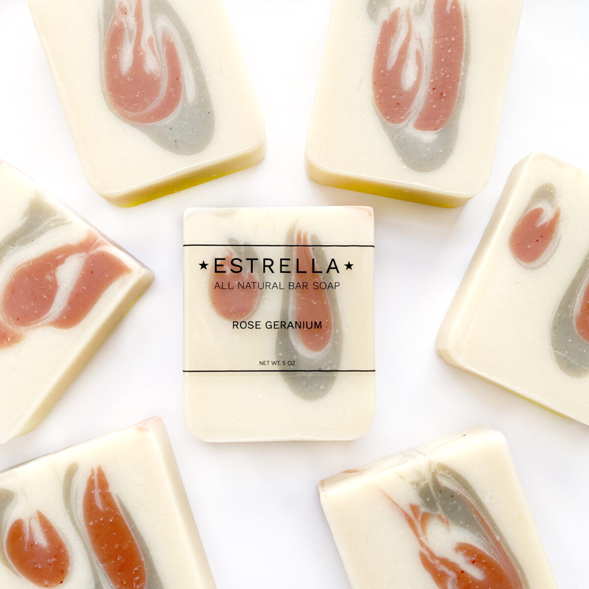 Handmade bar soaps with a swirled pattern of pink and white colors, labeled 'ESTRELLA' with 'ROSE GERANIUM' on the top bar.