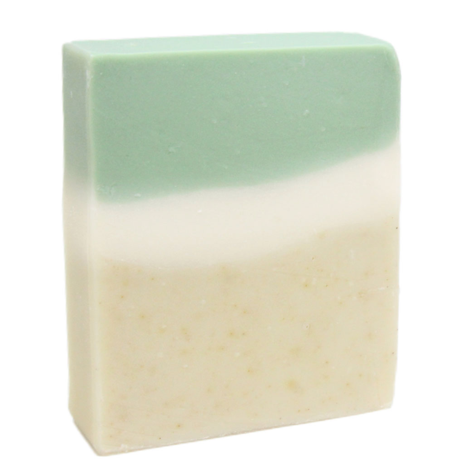 A bar of handmade soap with a gradient of light green to beige, marked with natural patterns from botanicals and clays.