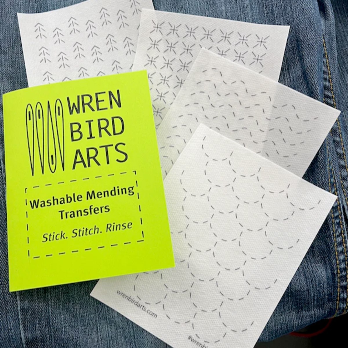 An example of each of the four sashiko design sheets are laid out on top of a pair of jeans. A neon green sheet with "Wren Bird Arts" logo is laid on top. 