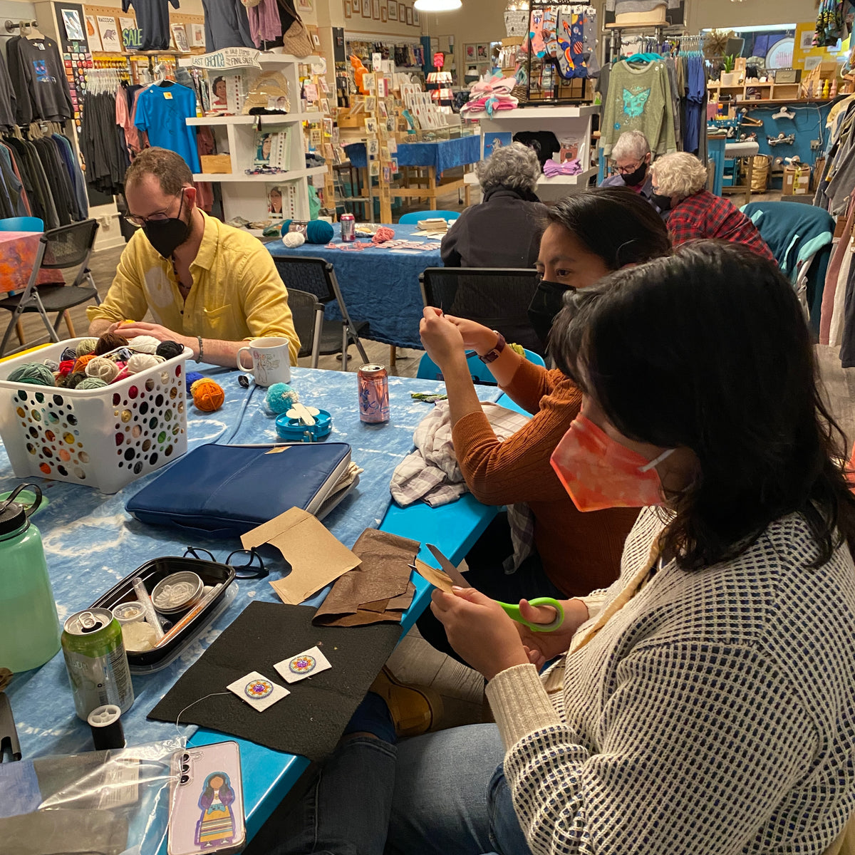People working on craft projects at a table in a store setting. 