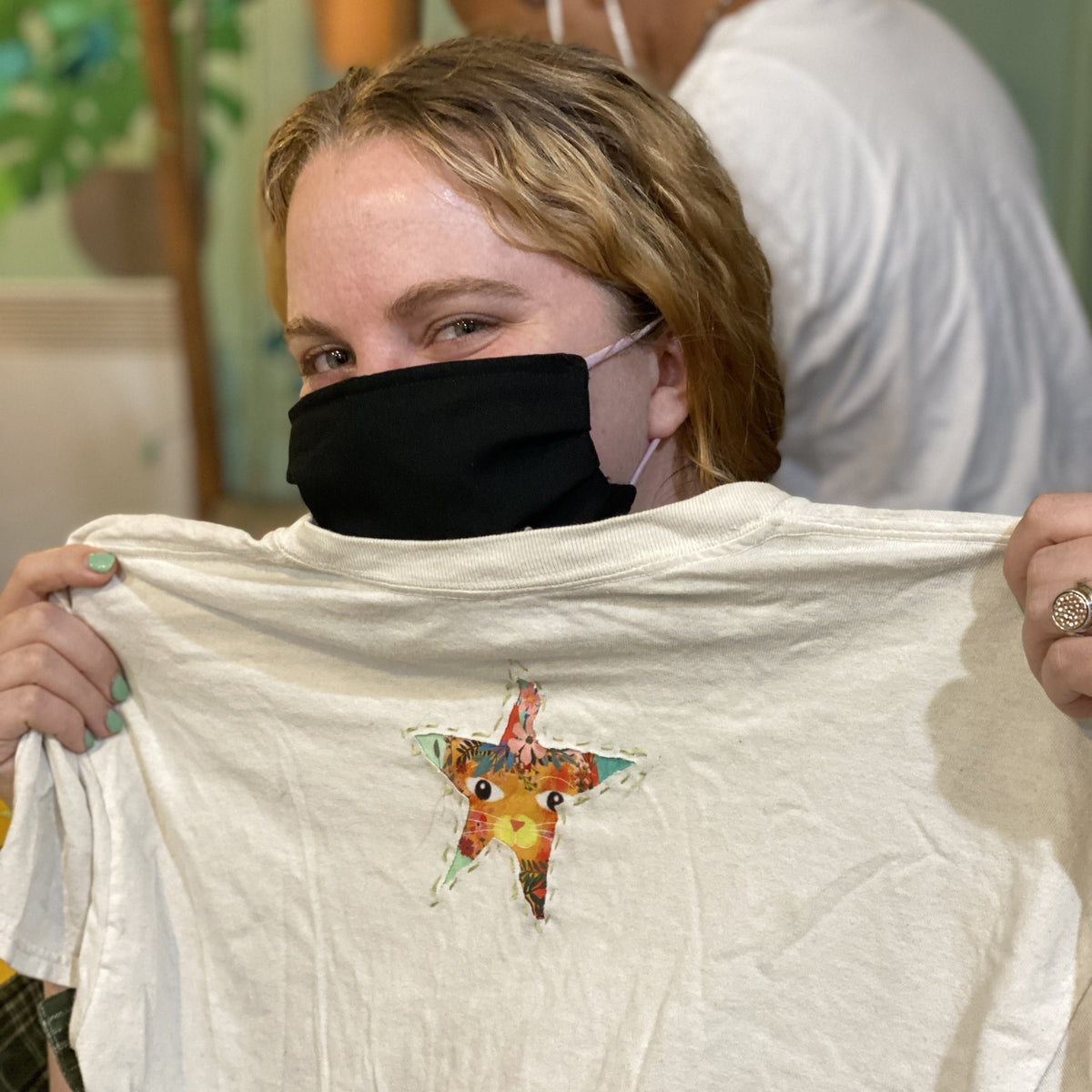 Person holding a white t-shirt with a colorful star reverse applique design.