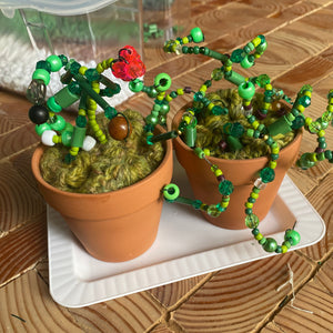 Two small potted plants with decorative green beaded branches on a wooden surface.
