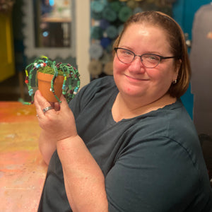 Person holding a beaded potted plant with decorative elements in an indoor setting. 
