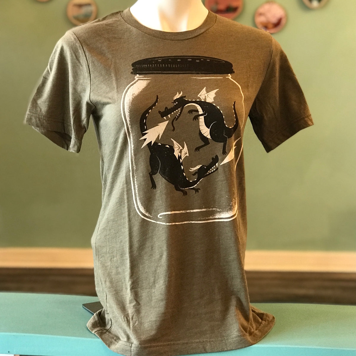 A shirt on a mannequin that shows two dragons with wings captured in a jar. Dragonflies. 