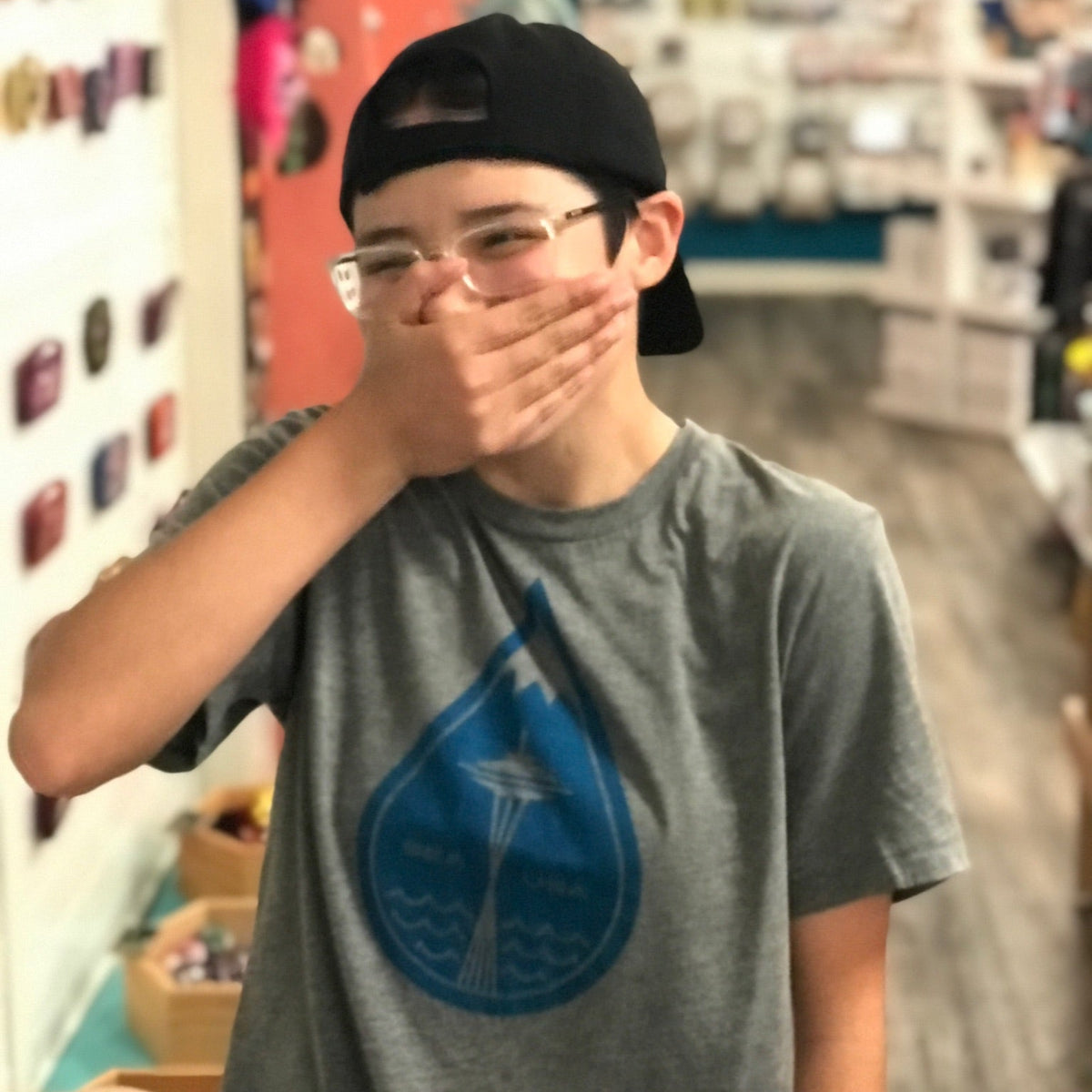 A person wearing a shirt with a big raindrop in the middle. The top of the raindrop looks like a mountain cap and there is a Space Needle in the middle. 