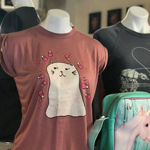 T-shirt with ghost cat design on a mannequin, next to a green bag with a pink unicorn design.