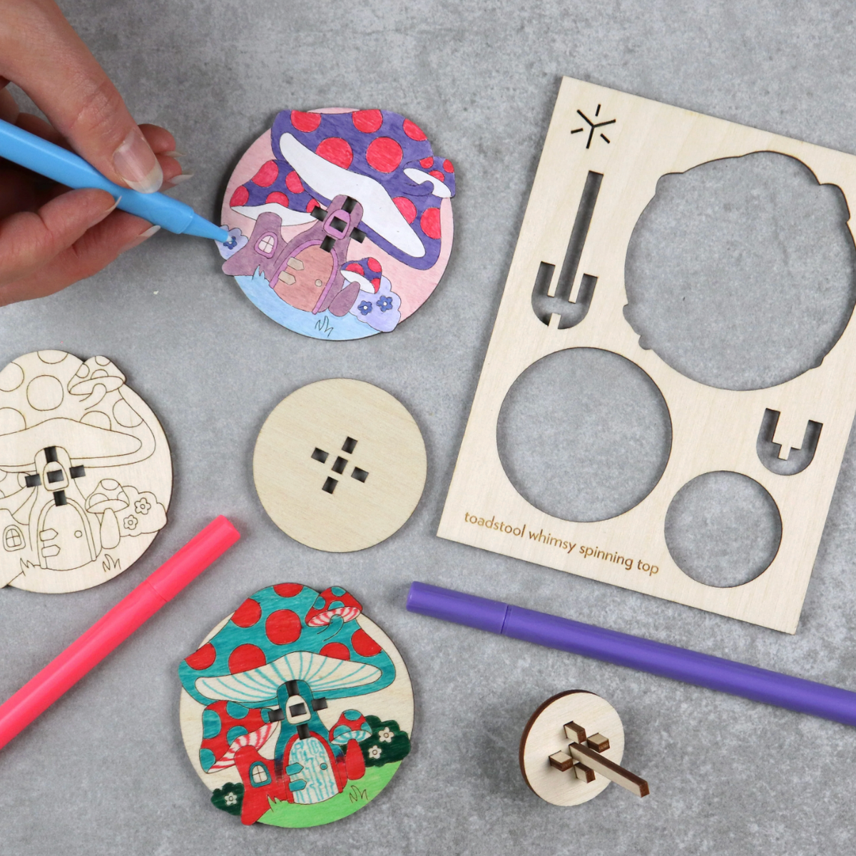 Wooden spinning tops with toadstools are being colored in with markers.