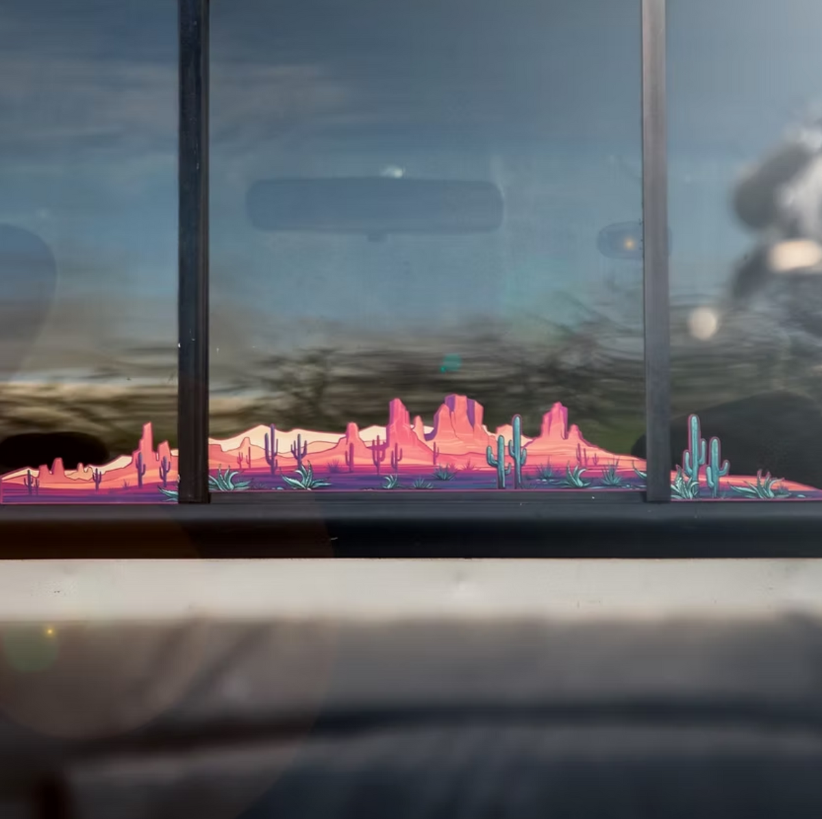 Window view of a desert landscape with cacti and mountains. 