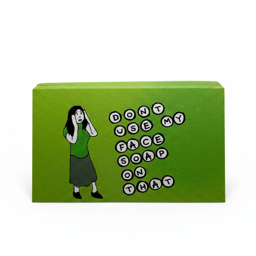 A green rectangular sticker standing upright on a white surface, featuring a cartoon woman in a green top and dark skirt next to the phrase 'DON'T USE MY FACE SOAP ON THAT' in black-and-white letter circles.