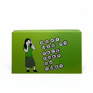 A green rectangular sticker standing upright on a white surface, featuring a cartoon woman in a green top and dark skirt next to the phrase 'DON'T USE MY FACE SOAP ON THAT' in black-and-white letter circles.