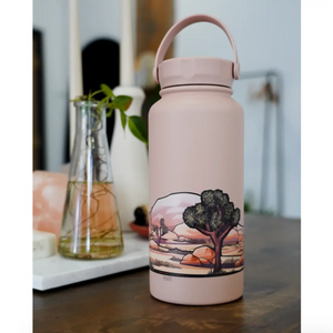 Pink water bottle with a Joshua Tree desert landscape design on a wooden surface.
