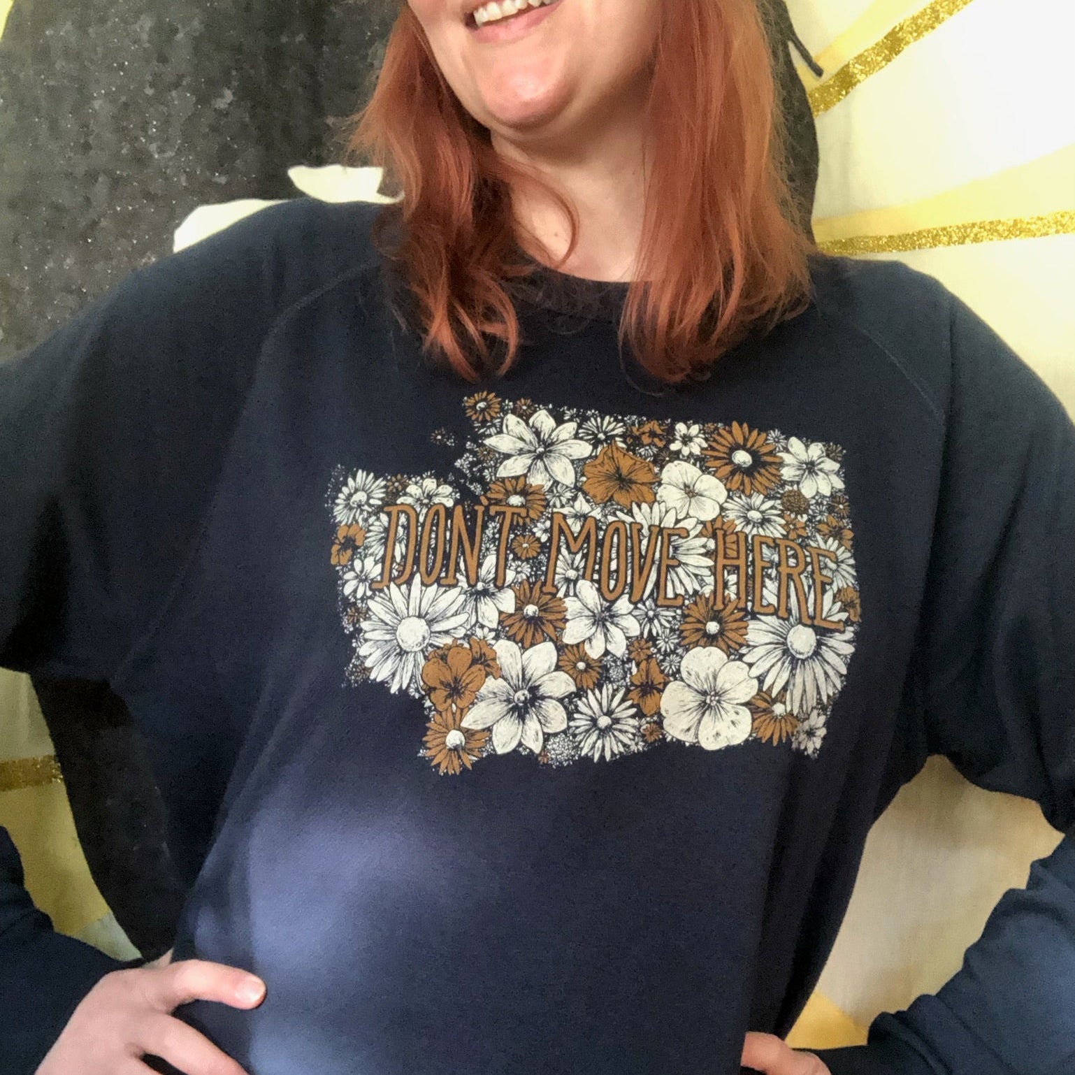 Person wearing a navy blue sweatshirt with floral design and text that says, "Don't move here."