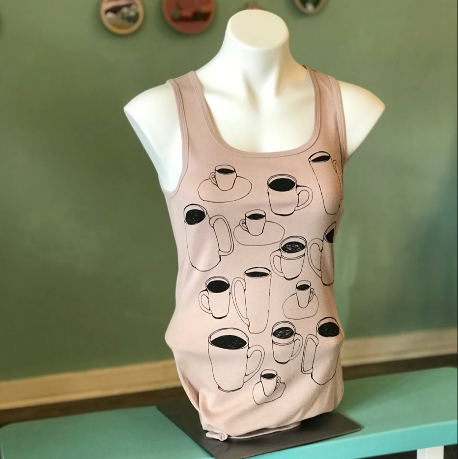 Heather pink tank top with coffee cup designs on a mannequin against a green wall.