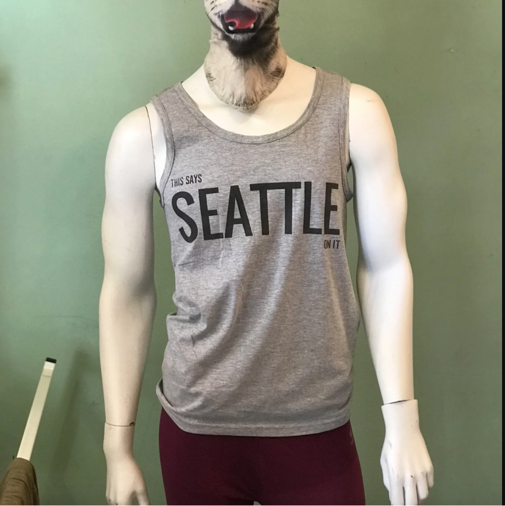 Mannequin wearing a gray tank top with 'THIS SAYS SEATTLE ON IT' text against a green background.