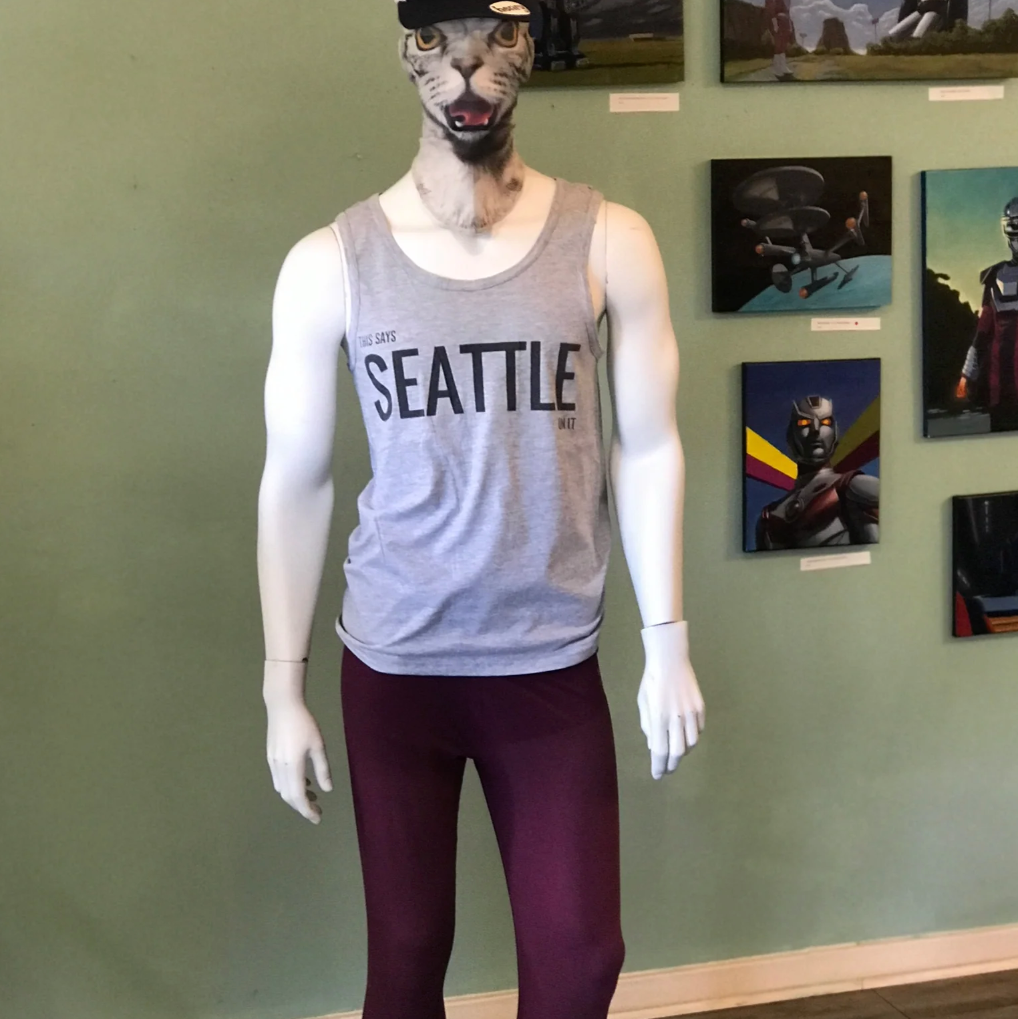 Mannequin wearing a 'Seattle' tank top in front of a wall with framed pictures.