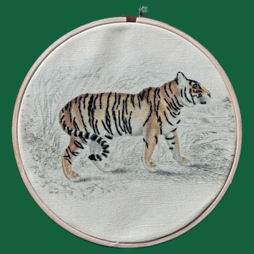 Embroidery of a tiger in a hoop on a textured fabric background. 