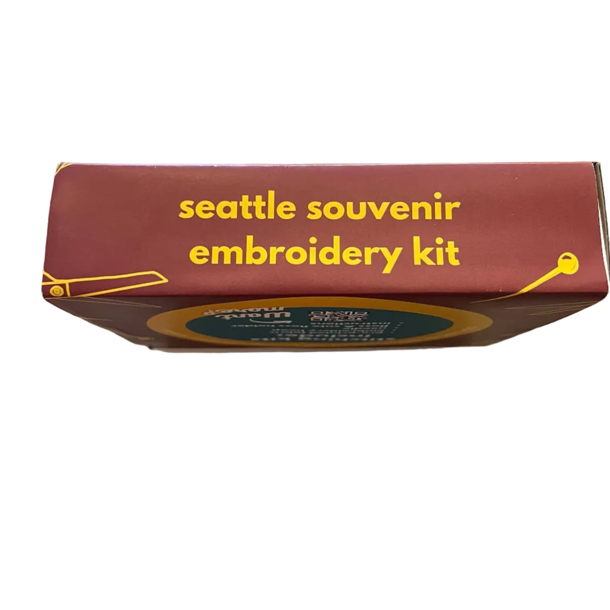 A red rectangular box labeled 'seattle souvenir embroidery kit' in yellow text, photographed from above.