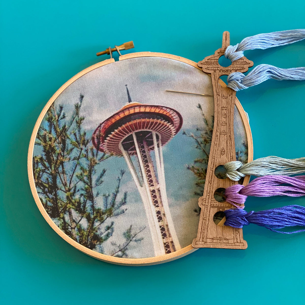 Embroidery hoop with a space needle design on a teal background. 