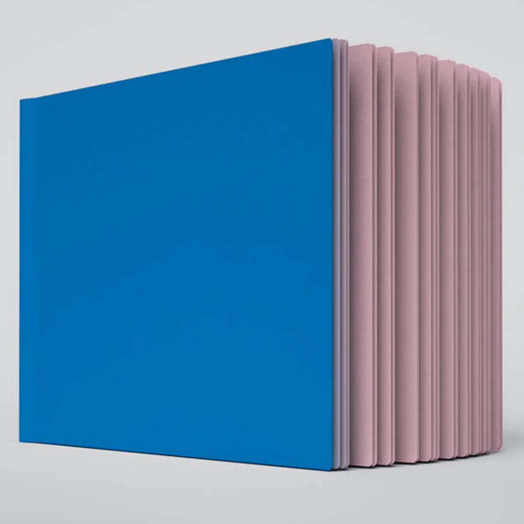 A close up photo of the Pluto ugly book sketchbook. The cover is blue and the pages are light pink colored.