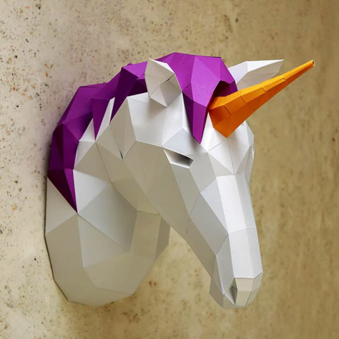 Example of a unicorn paper craft kit completed and hung on a textured cream colored wall.