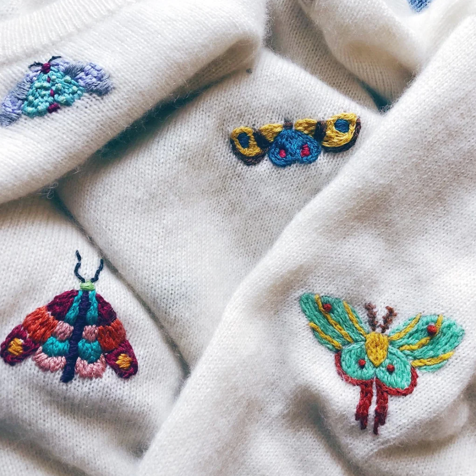 Examples of different moth embroidery patterns stitched up onto an off white sweater.