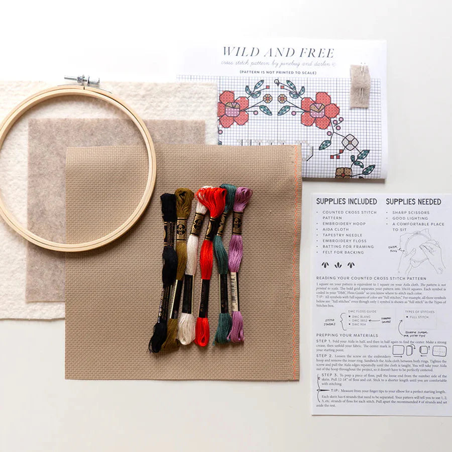 A photo shot from above of all the items included in the Wild and Free cross stitch kit. You get an embroidery hoop, backing felt, aida fabric, embroidery floss, pattern and hand illustrated instructions.