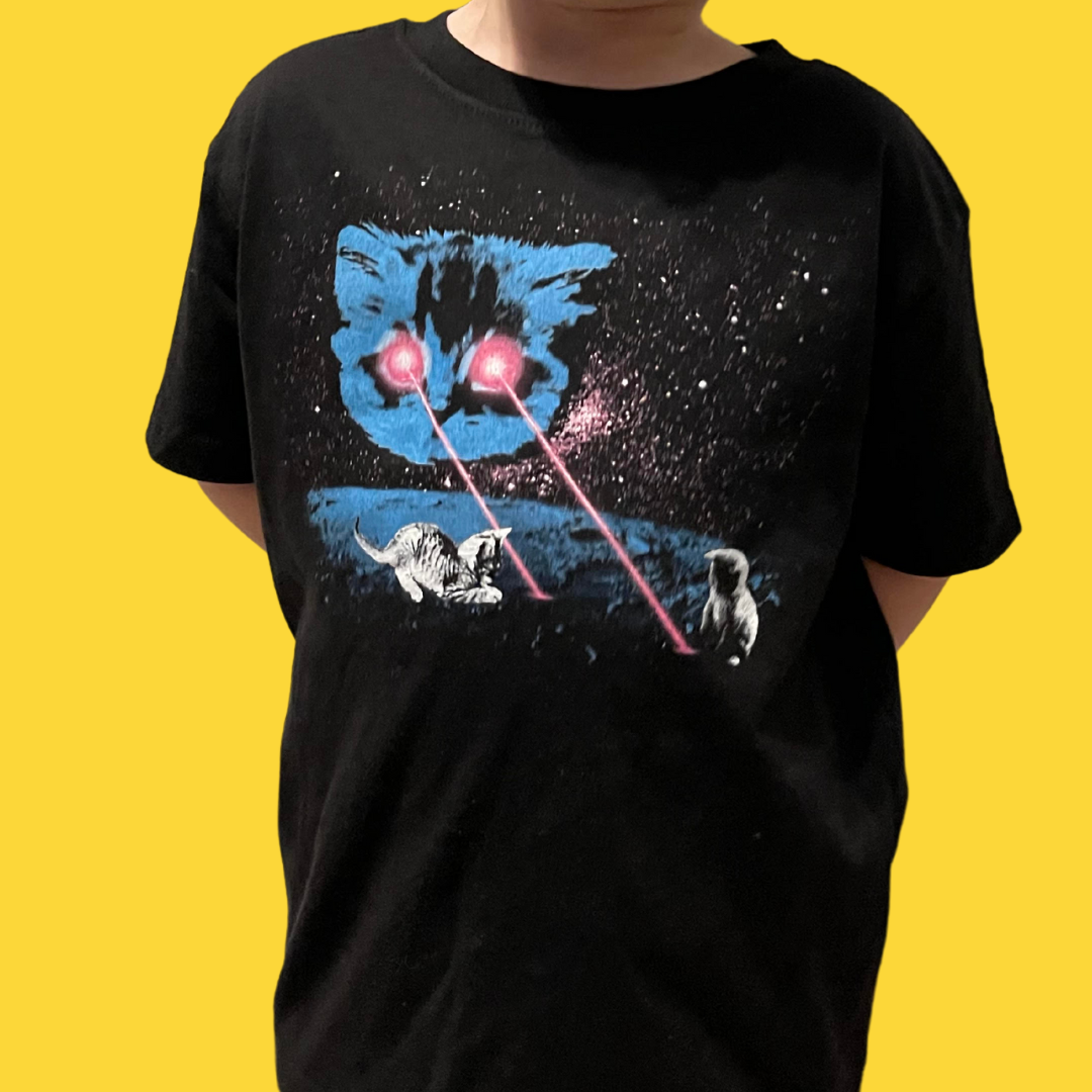 Young person wearing a black tshirt with a large blue cat on it. The cat is shooting hot pink lasers out of his eyes and there are tiny kittens playing in the lasers. 