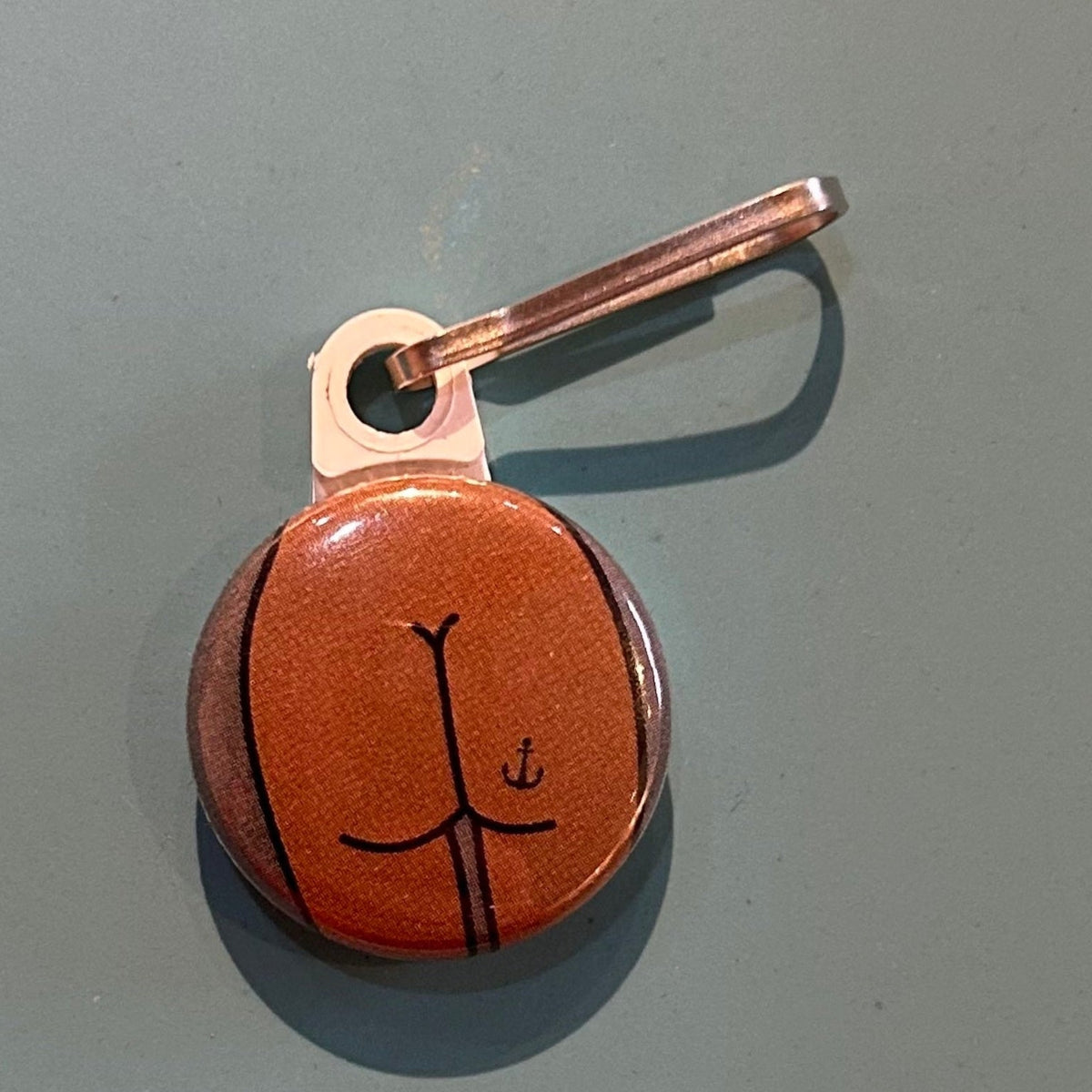Zipper pull with a flat butt design with an anchor tattoo on a gray background. 