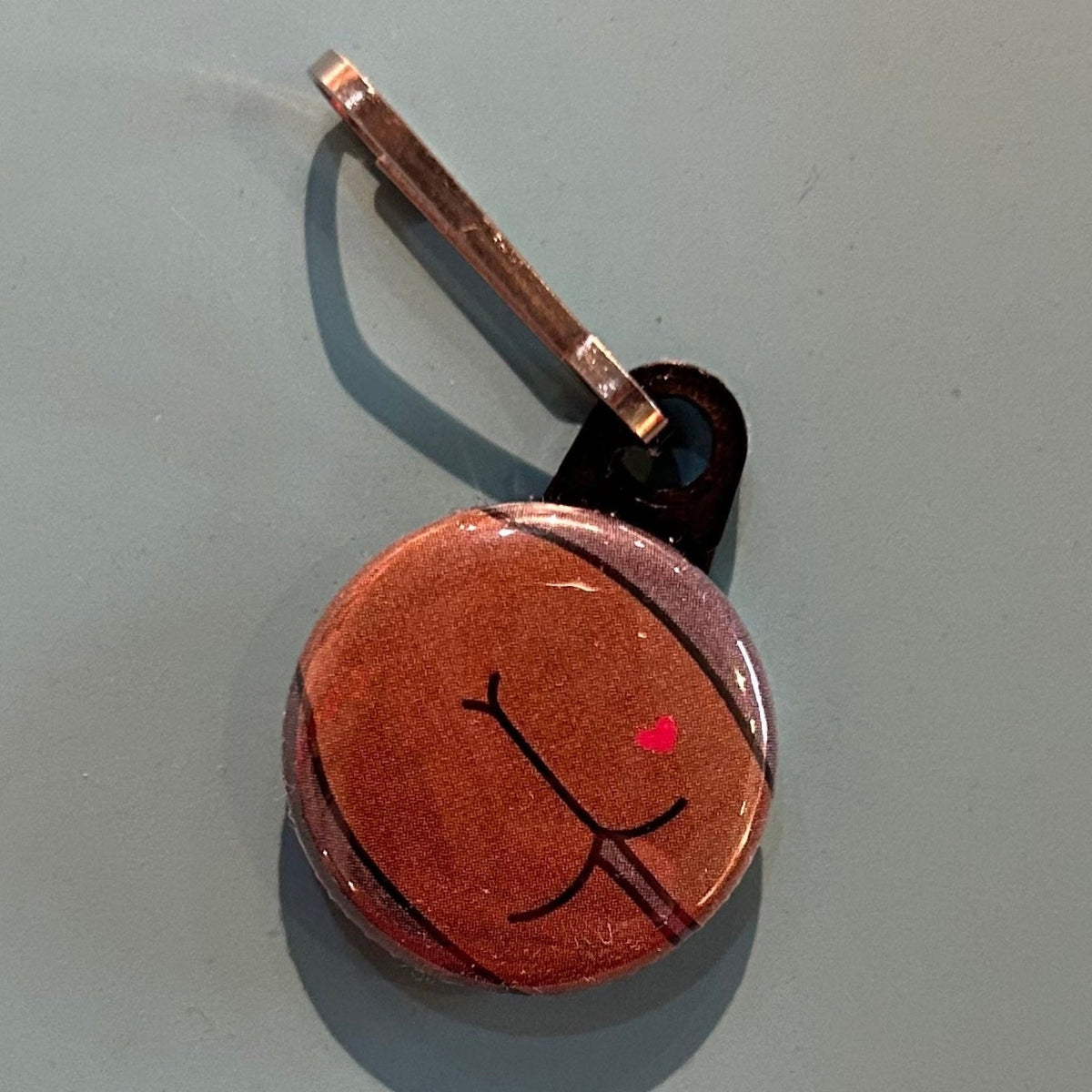 Small zipper pull with a flat butt with a heart tattoo on a light gray background. 