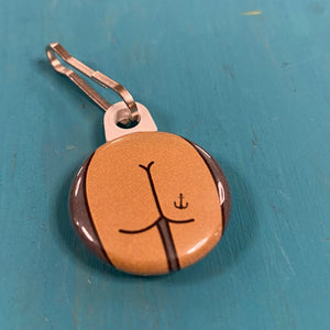 Zipper pull with a thin butt with an anchor tattoo against a blue background.